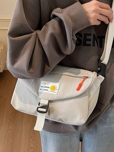 Borsa a tracolla in nylon beige con patta ed etichette street style indossata da un modello