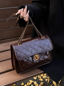 Quilted dark brown chain bag in glossy leather with gold hardware on wooden bench