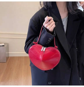 Detail of red heart-shaped leather crossbody bag carried by model in black suit