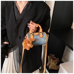 Détail du mini sac Boston en denim bleu avec finitions en cuir marron et breloque ours