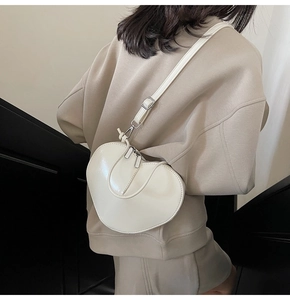 Detail of off-white heart-shaped crossbody bag with dual zippers and leather strap on model