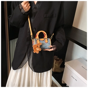 Détail du mini sac Boston en denim marine avec finitions en cuir marron et bijou ours