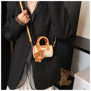 Détail d'un mini sac Boston en cuir crème avec pendentif ours et finitions métalliques