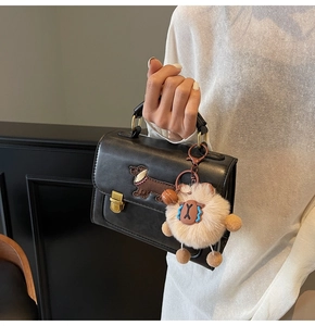 Detail of black crossbody bag featuring dachshund embroidery and a beige plush sheep charm