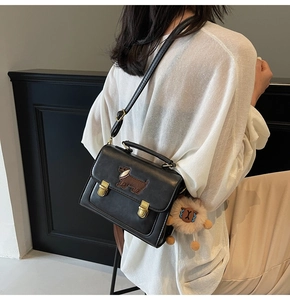 Detail of black faux leather square bag featuring embroidered dachshund and plush pompom charm