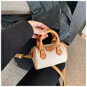 Détail du mini sac cylindre beige avec poignées brunes et accents de peinture rouge