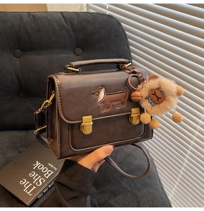 Close-up of retro brown PU leather satchel with dog embroidery and plush doll charm