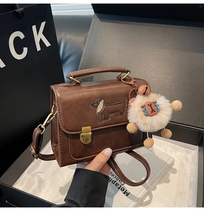 Detail of dark brown leather handbag featuring dachshund embroidery and plush charm