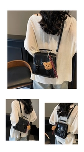 Detail of black faux leather bag with double buckle straps and a cute brown bear charm