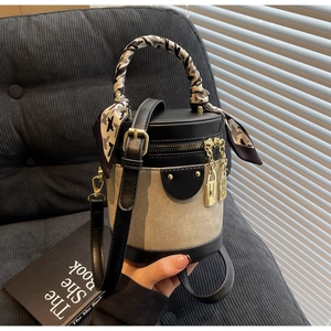 Detail of a contrast color cylinder bag featuring silk scarf handle and gold locks