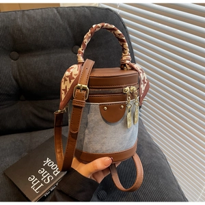 Detail of a denim cylindrical bag with brown leather trim and silk scarf handle