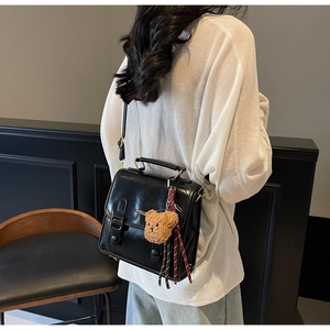 Detail of minimalist black leather shoulder bag with bear charm and striped ribbon accent