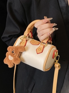Mini sac Boston crème avec poignées camel, bords rouges contrastés et un pendentif ours
