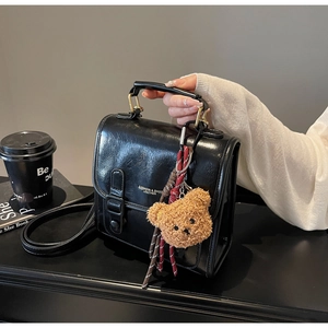 Close-up of black retro square handbag with a plush teddy bear charm and metal buckle lock