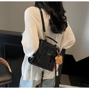 Detail of black leather backpack with flap double buckles and cute teddy bear pendant