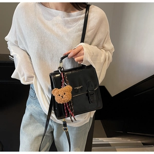 Detail of black faux leather shoulder bag with buckle strap and brown plush bear charm