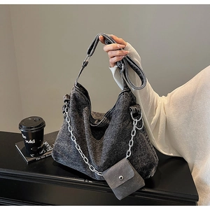 Close-up of washed denim tote with adjustable strap, metal chain, and mini pouch accessory