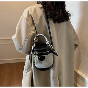 Close-up of contrast color cylinder bag with silk scarf handle and metal lock detail