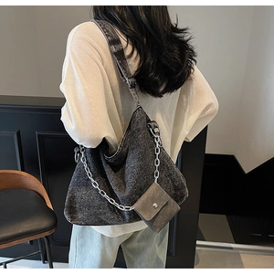 Detailed macro view of dark denim hobo bag featuring rugged silver metal chain and mini pouch
