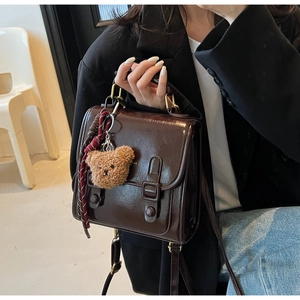 Detailed close-up of dark brown vintage PU leather messenger bag with plush bear pendant