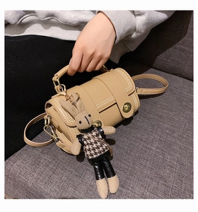 Close-up of beige cylindrical handbag with gold lock and cute bunny charm on sofa
