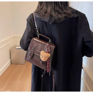 Deep brown glossy leather crossbody bag shown on model with teddy bear and tassel