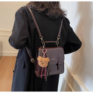 Detail of dark brown glossy patent leather mini backpack with golden metal accents and bear charm