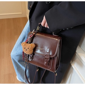 Close-up of brown leather shoulder bag with vintage buckles and teddy bear charm