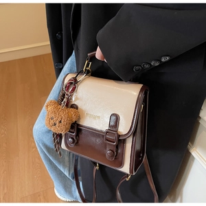 Detail of vintage two-tone messenger bag with buckle straps and a cute plush bear charm
