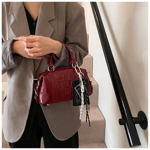 Detail of burgundy Boston bag featuring embossed Collective logo and woven rope charm