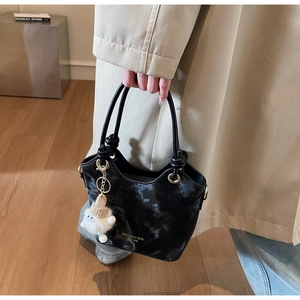 Détail du sac seau noir avec texture brillante, œillets dorés et décor de charme en peluche