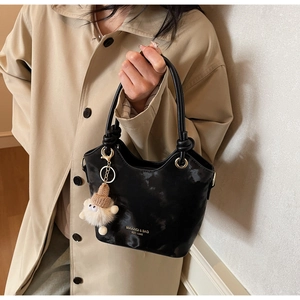 Détail du sac seau noir avec texture brillante, poignée nouée et finitions dorées
