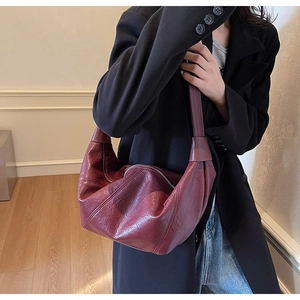 Detail of wine red pleated leather dumpling bag worn as a shoulder bag under the arm