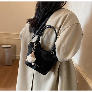 Détail d'un sac seau noir avec un charme en peluche blanc et un logo argenté sur cuir mat