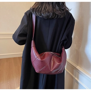 Deep burgundy leather dumpling bag worn underarm over a classic black wool coat