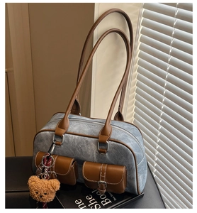 Detailed shot of retro denim shoulder bag with brown leather trim and cute plush bear charm