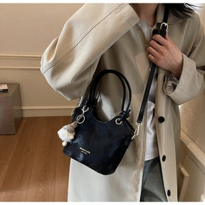 Détail d'un sac seau noir en cuir avec lettrage doré et un pompon blanc doux