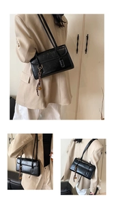 Detail of black glossy shoulder bag featuring gold ring buckle and elegant tassel charm