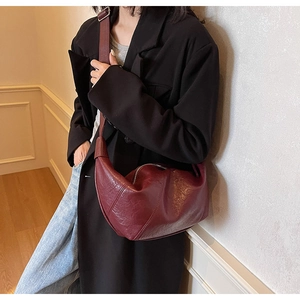 Detail view of burgundy crescent dumpling bag with pleated texture and adjustable strap
