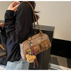 Close-up of vintage brown Boston bag with buckled pockets and a plush bear charm accessory