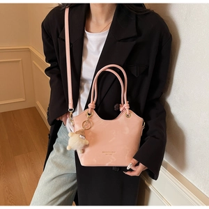 Détail d'un sac seau en cuir verni rose avec logo doré et breloque mouton en peluche