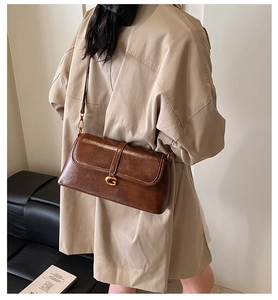 Detail view of a vintage brown leather crossbody bag with a gold G buckle on a trench coat