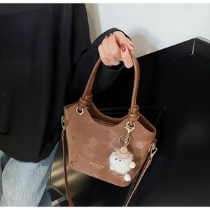 Détail d'un sac seau marron avec une peluche blanche et une bandoulière réglable
