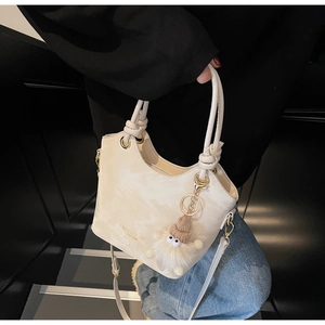 Détail du sac seau crème avec un pendentif en peluche et un logo métallique