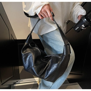 Detail of black leather dumpling bag featuring knotted shoulder strap and curved fold design