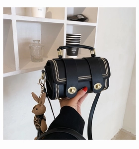 Detail of black crossbody bag with gold studs, metal ring buckle, and cute bunny pendant