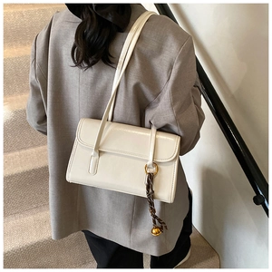Detail of white glossy underarm bag featuring a gold ring and braided rope charm