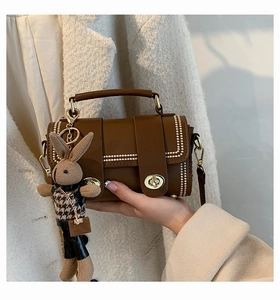 Detail of a brown leather handbag with gold studs and a cute woven bunny keychain