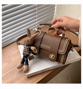 Detail view of brown cylinder bag with gold lock and cute knitted rabbit charm accessory