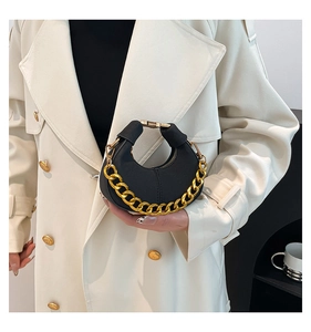 Detalle del bolso de media luna negro con cadena dorada sobre una gabardina beige